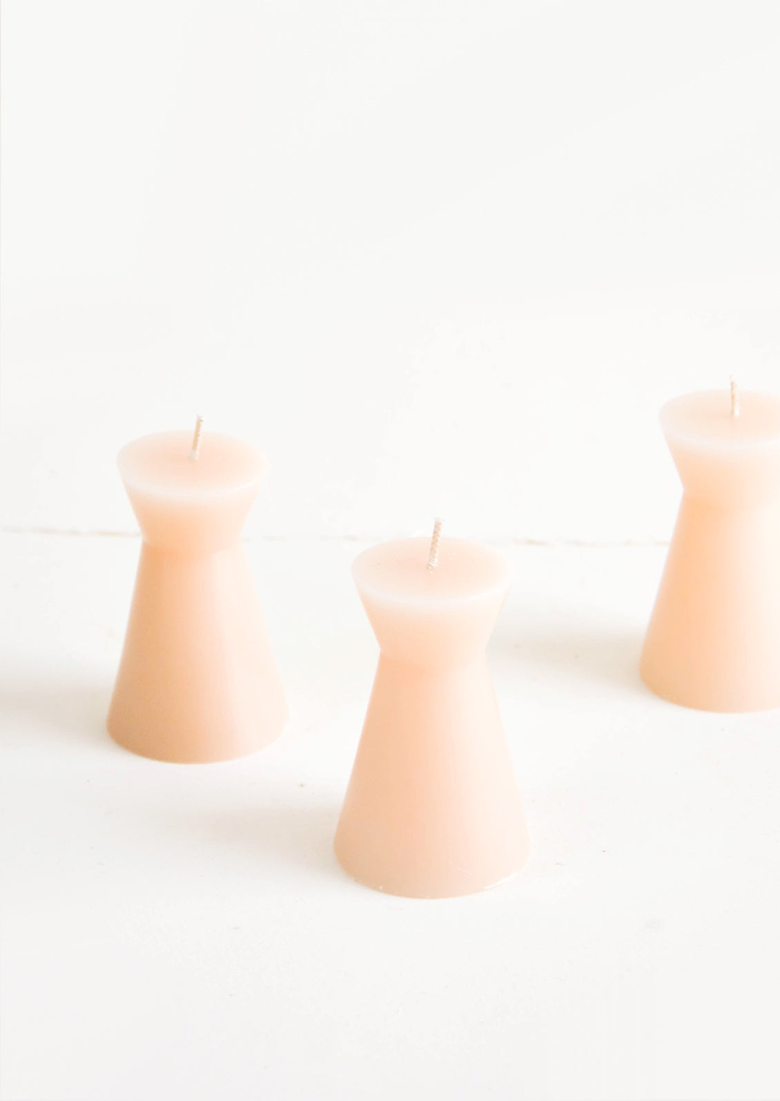 Small, tapered geometric votive candles in peach color