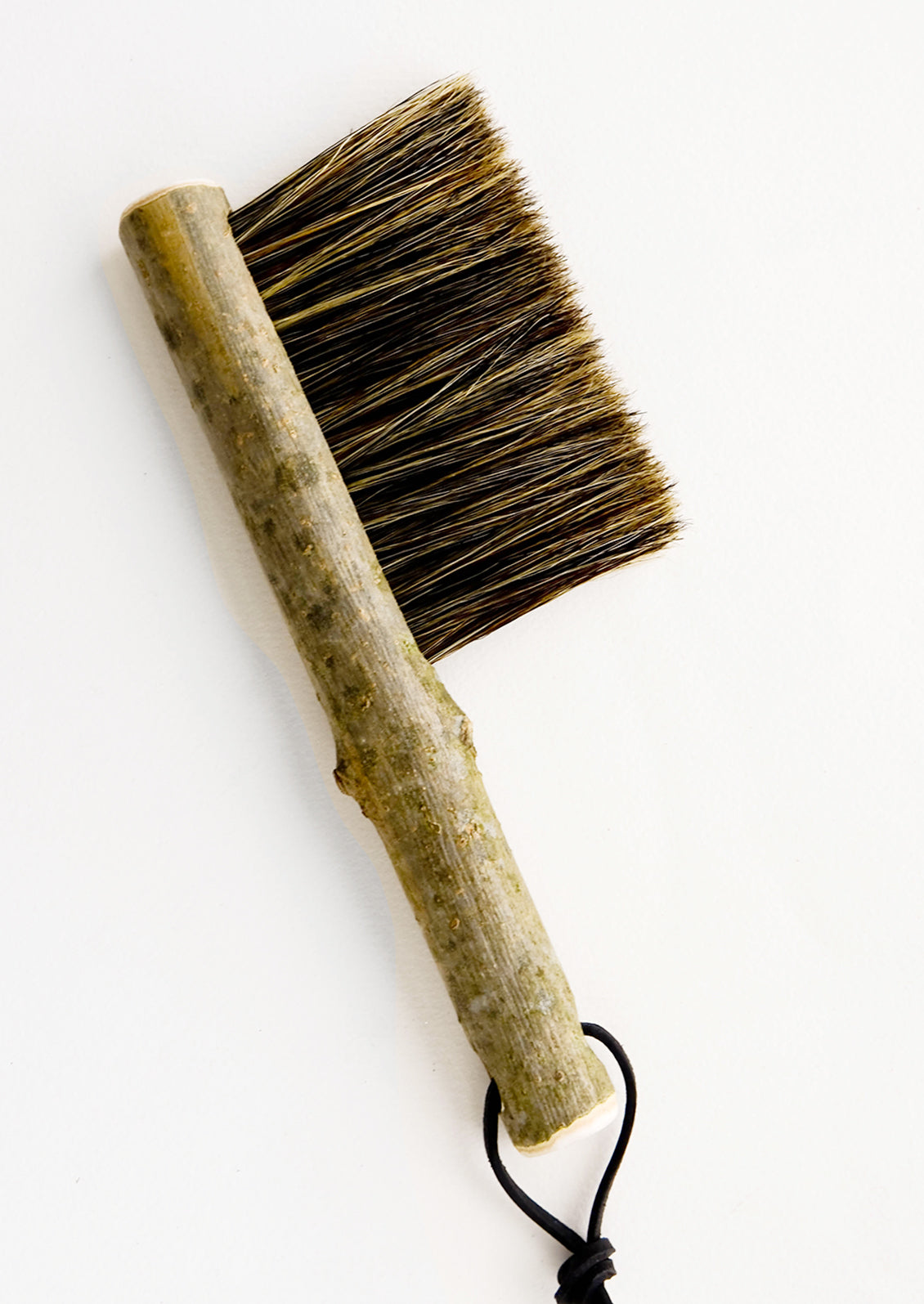 Bristle brush with natural bark handle and leather tie at end