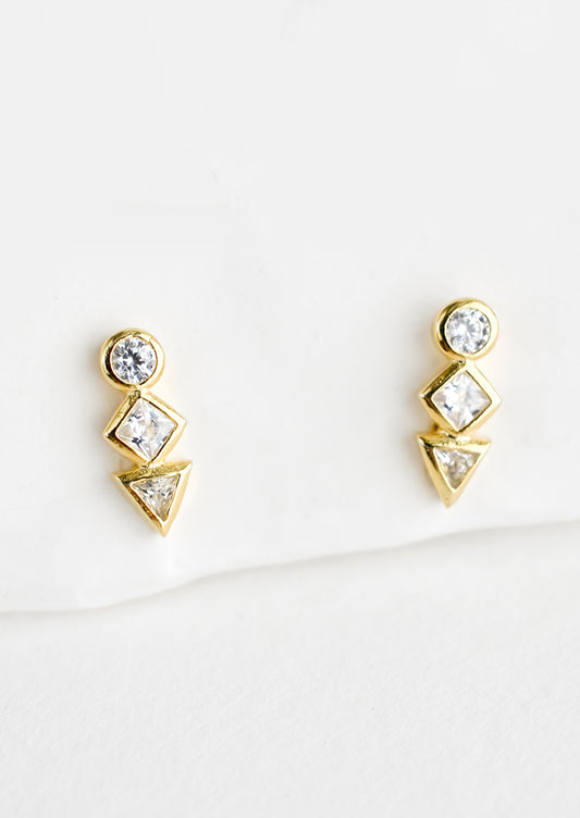 A pair of gold stud earrings with a circle, diamond and triangle crystal stacked in a row.