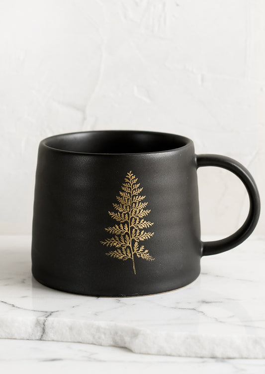 A black ceramic mug with single gold fern print.