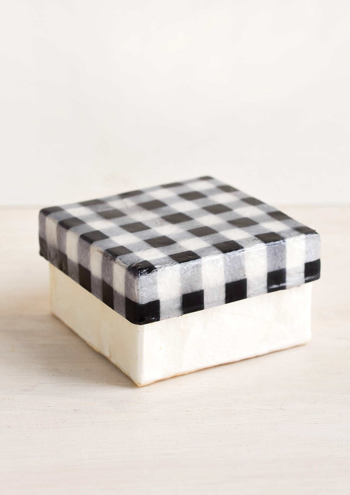 A small square box made from capiz with black and white gingham patterned lid.