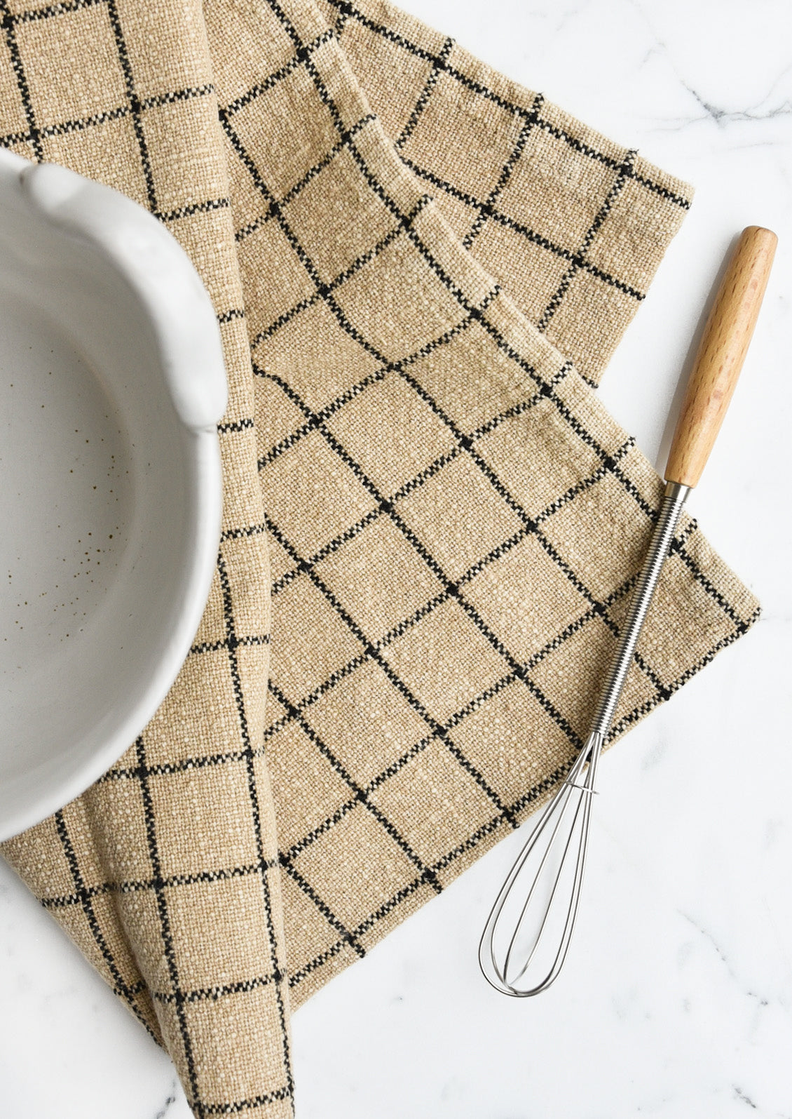 A sepia toned tea towel with black grid pattern folded under a bowl with a whisk