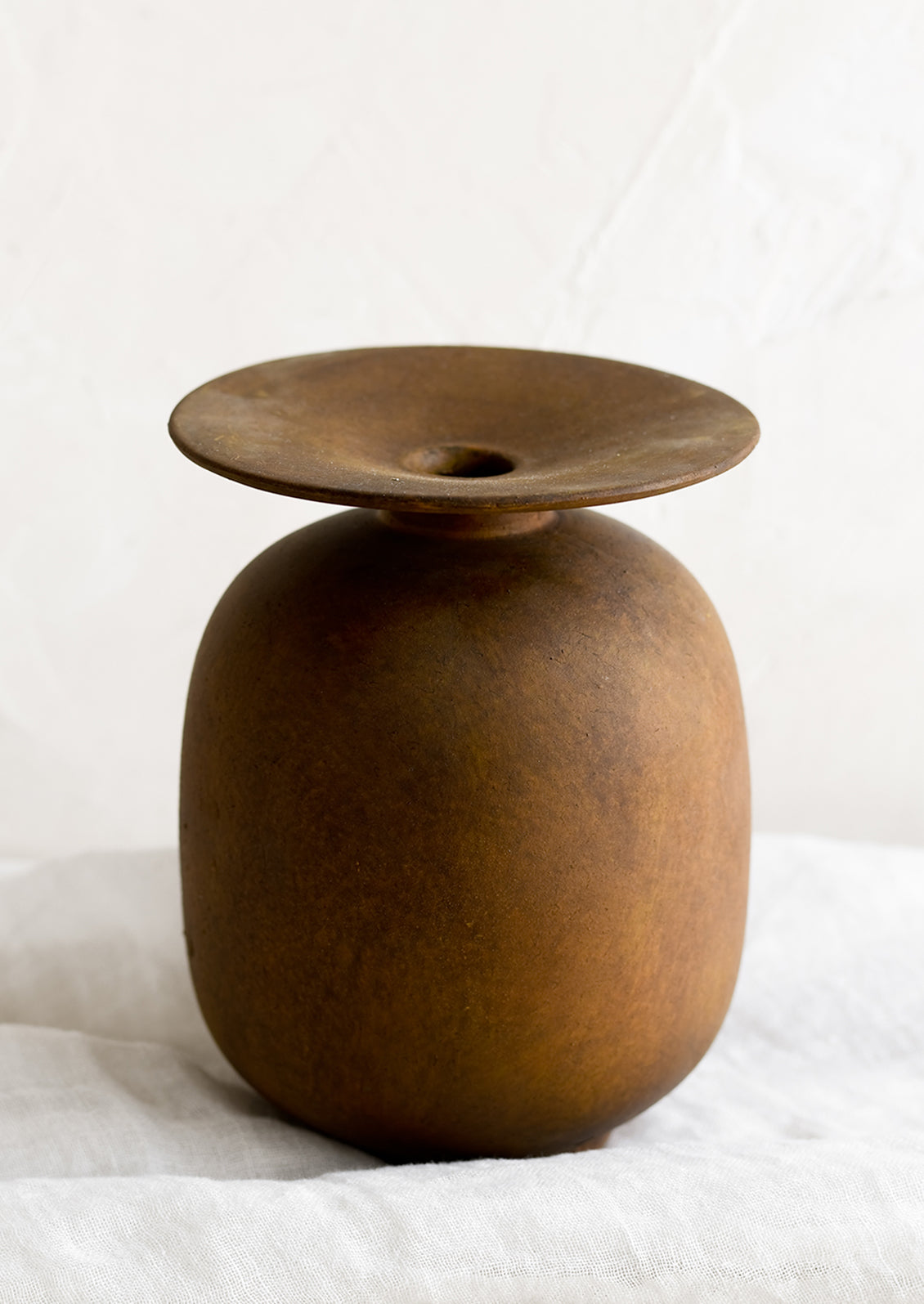 A brown distressed ceramic vase with saucer-like top.