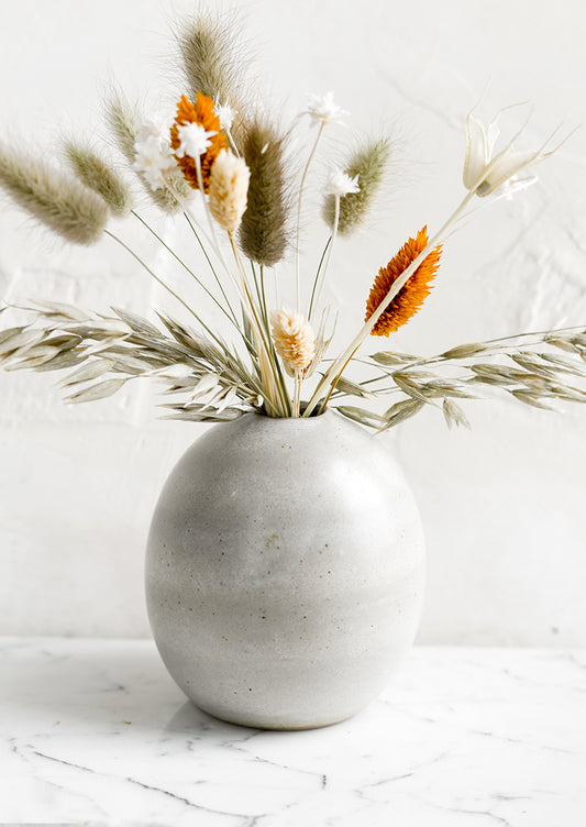 A ceramic bud vase with dried flowers.
