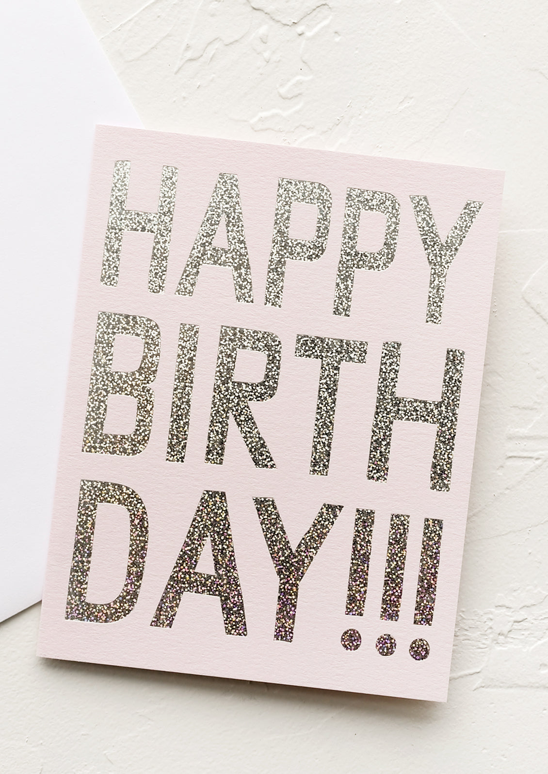 A pale pink birthday card with silver holographic glitter text reading "Happy birthday!!!"