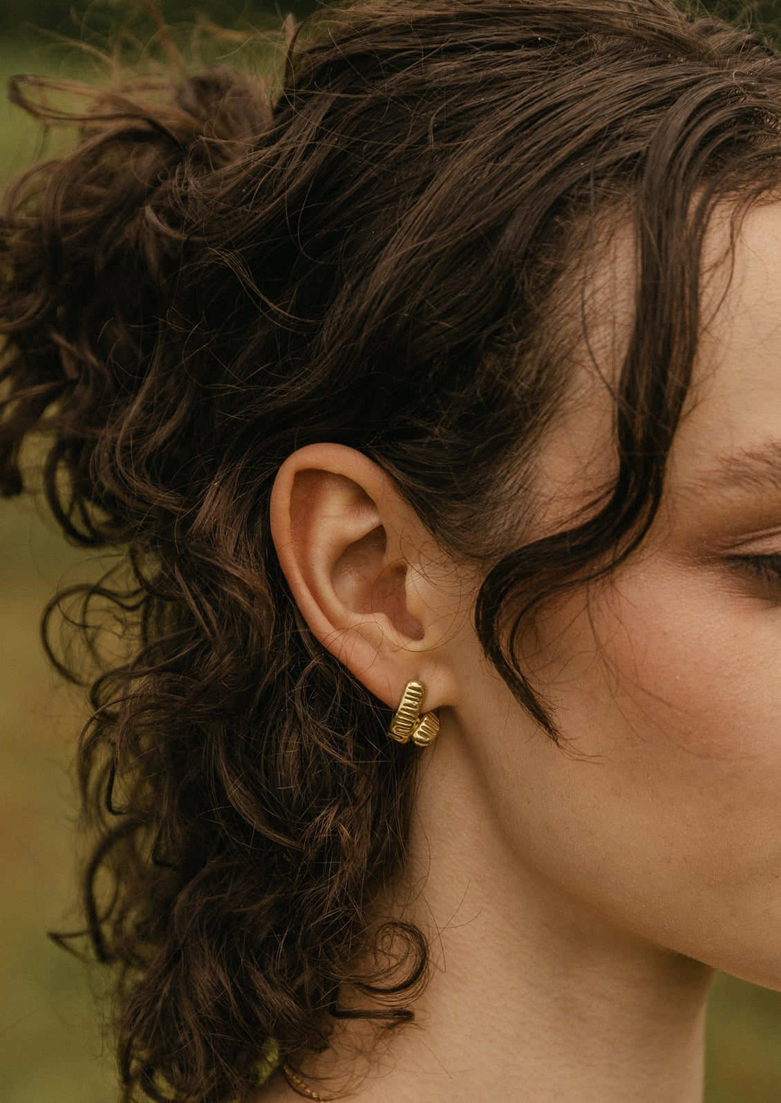 A woman wearing a pair of brass earrings.