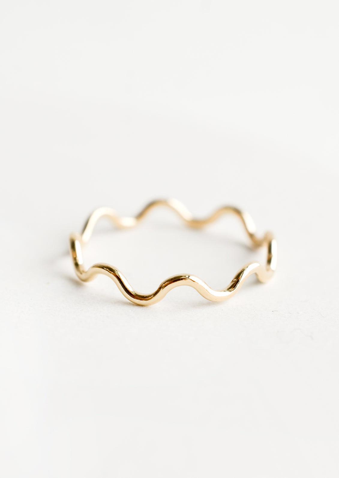 A gold stacking ring in curvy ripple shape.