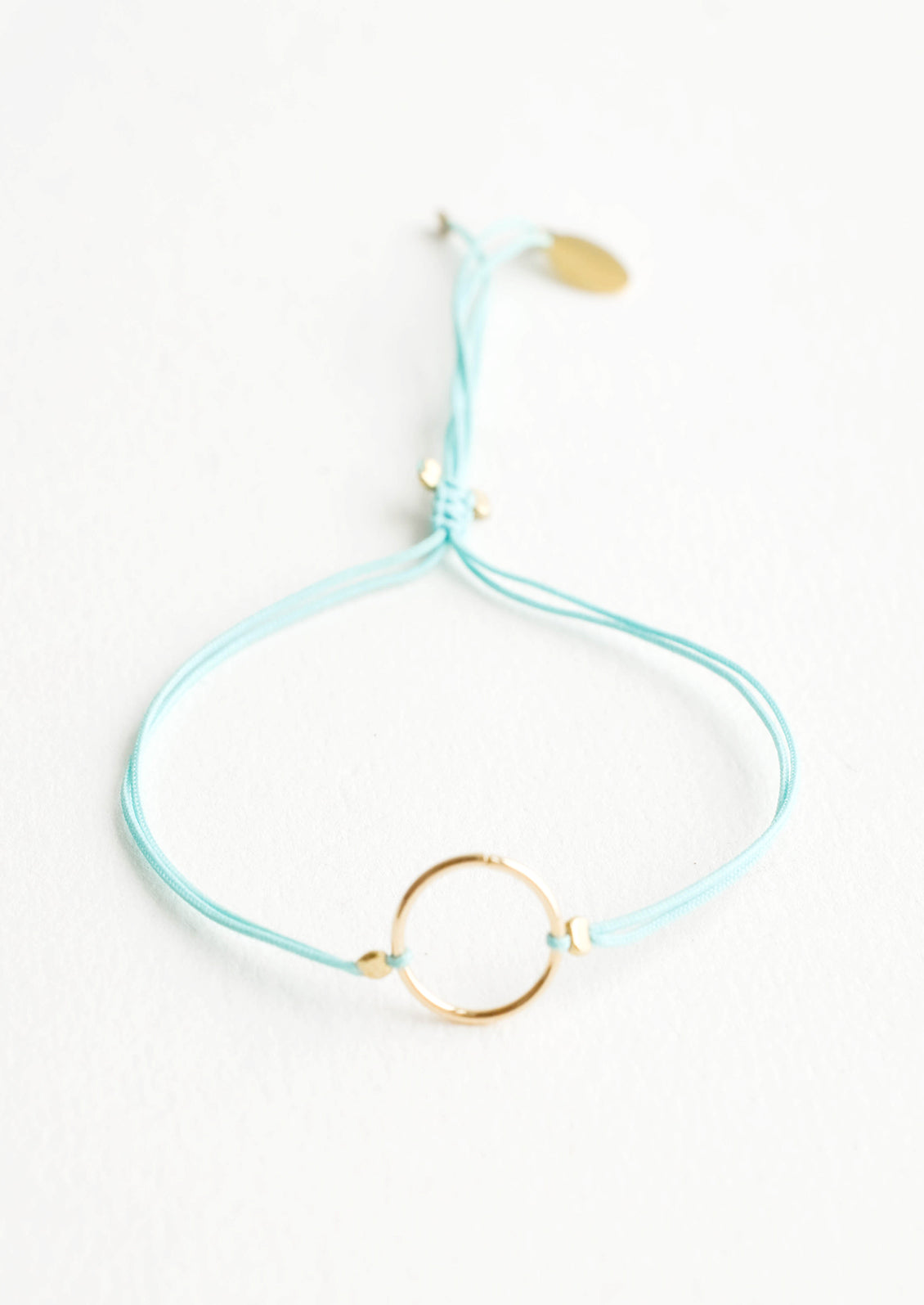 Bracelet with yellow gold circle charm centered on an adjustable aqua string.