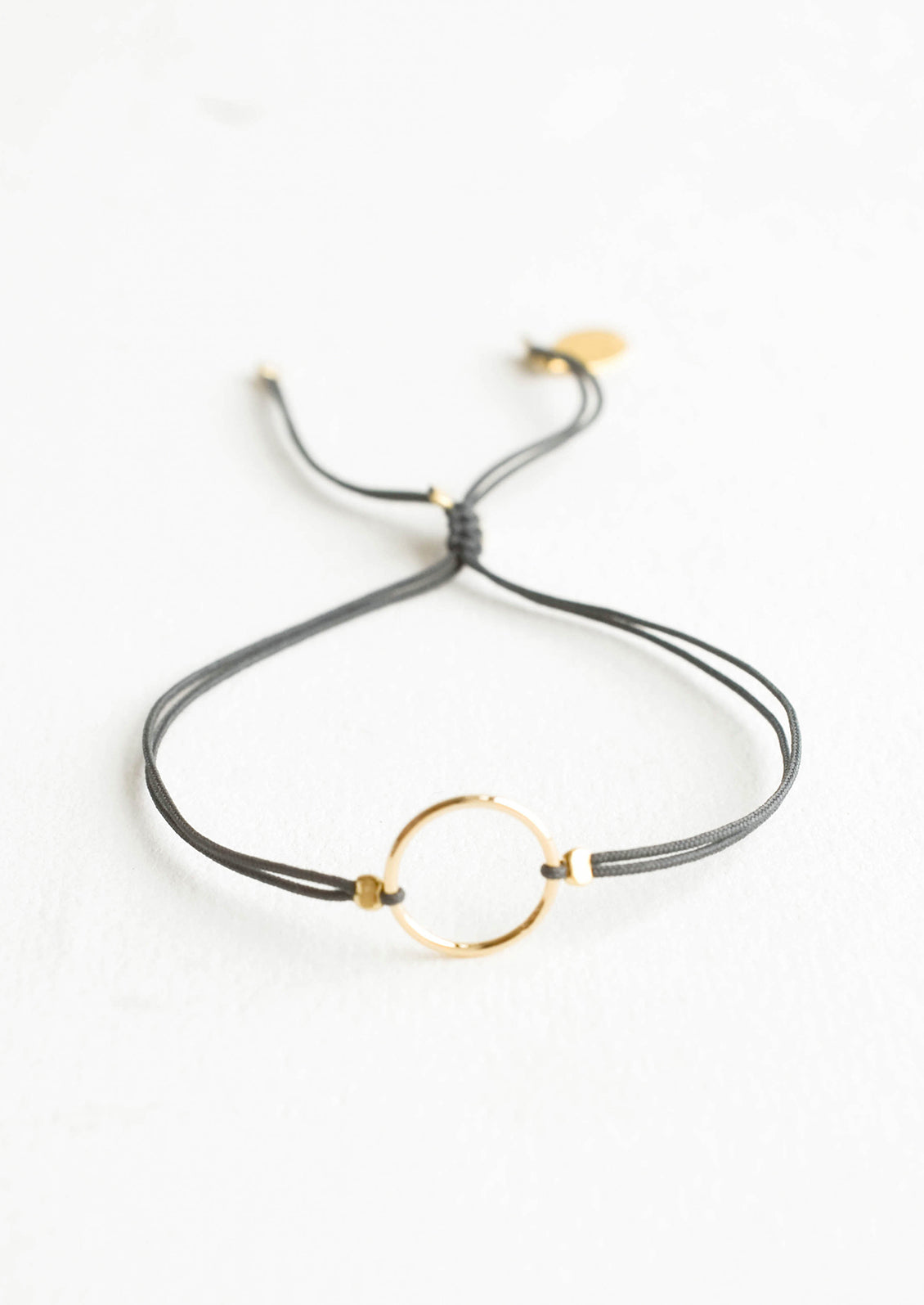 Bracelet with yellow gold circle charm centered on an adjustable dark grey string.