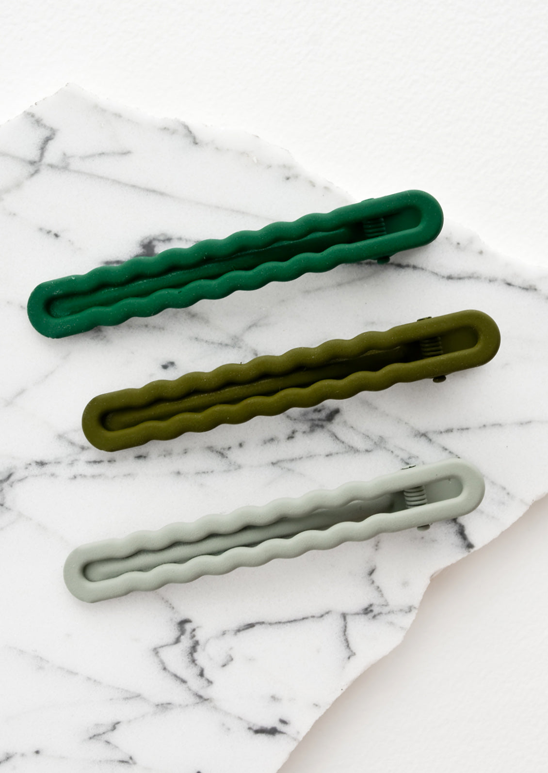 Three hair clips with wavy squiggle design in gradient green hues.