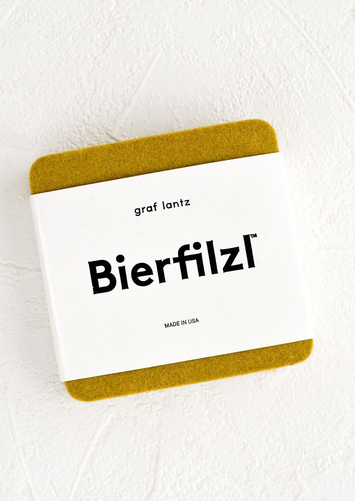 A package of square wool felt coasters in ochre.
