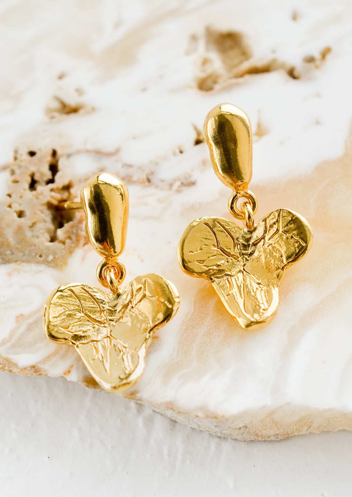 A pair of gold post back earrings in grape leaf shape.