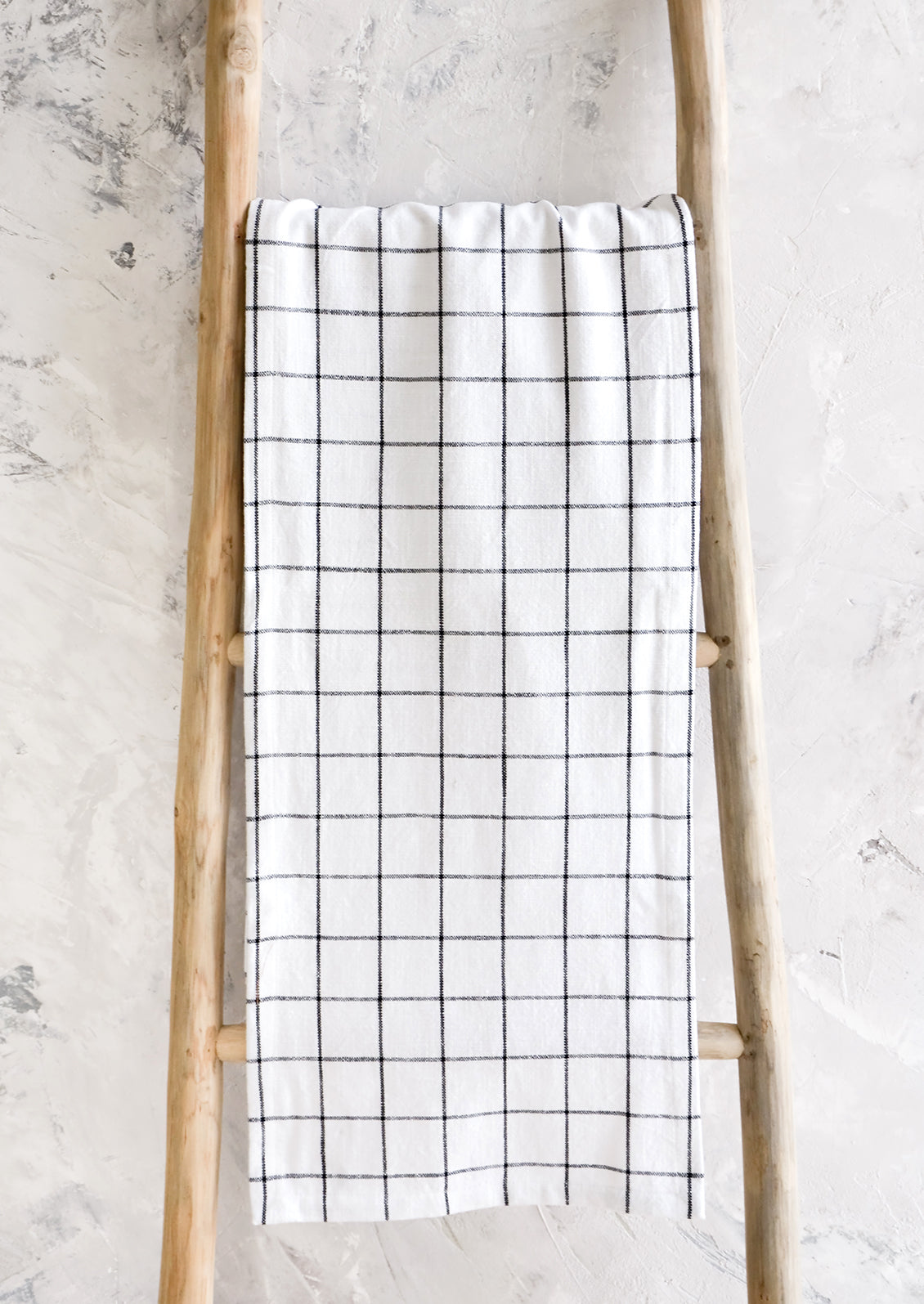 White cotton table runner with black grid check print, hanging on display ladder