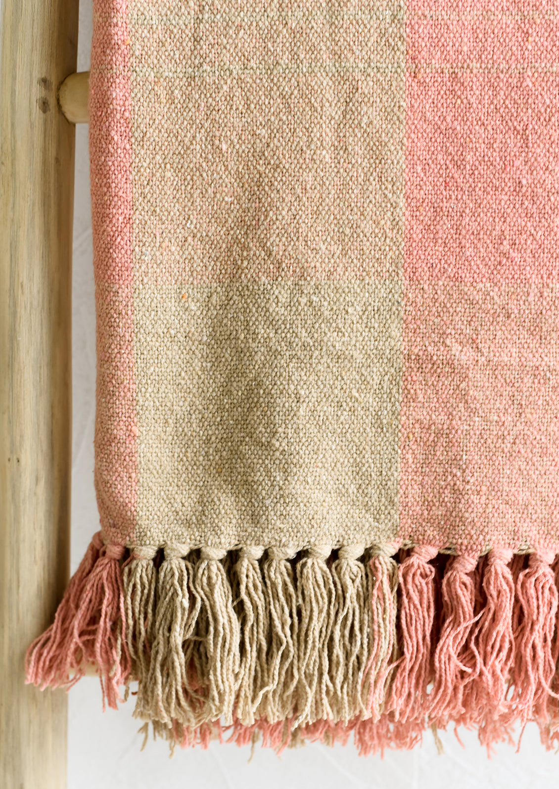 A cotton blank in peach and tan check pattern with fringe trim.