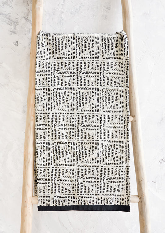 Table runner in natural cotton with black border and geometric print in black, displayed on a wooden ladder