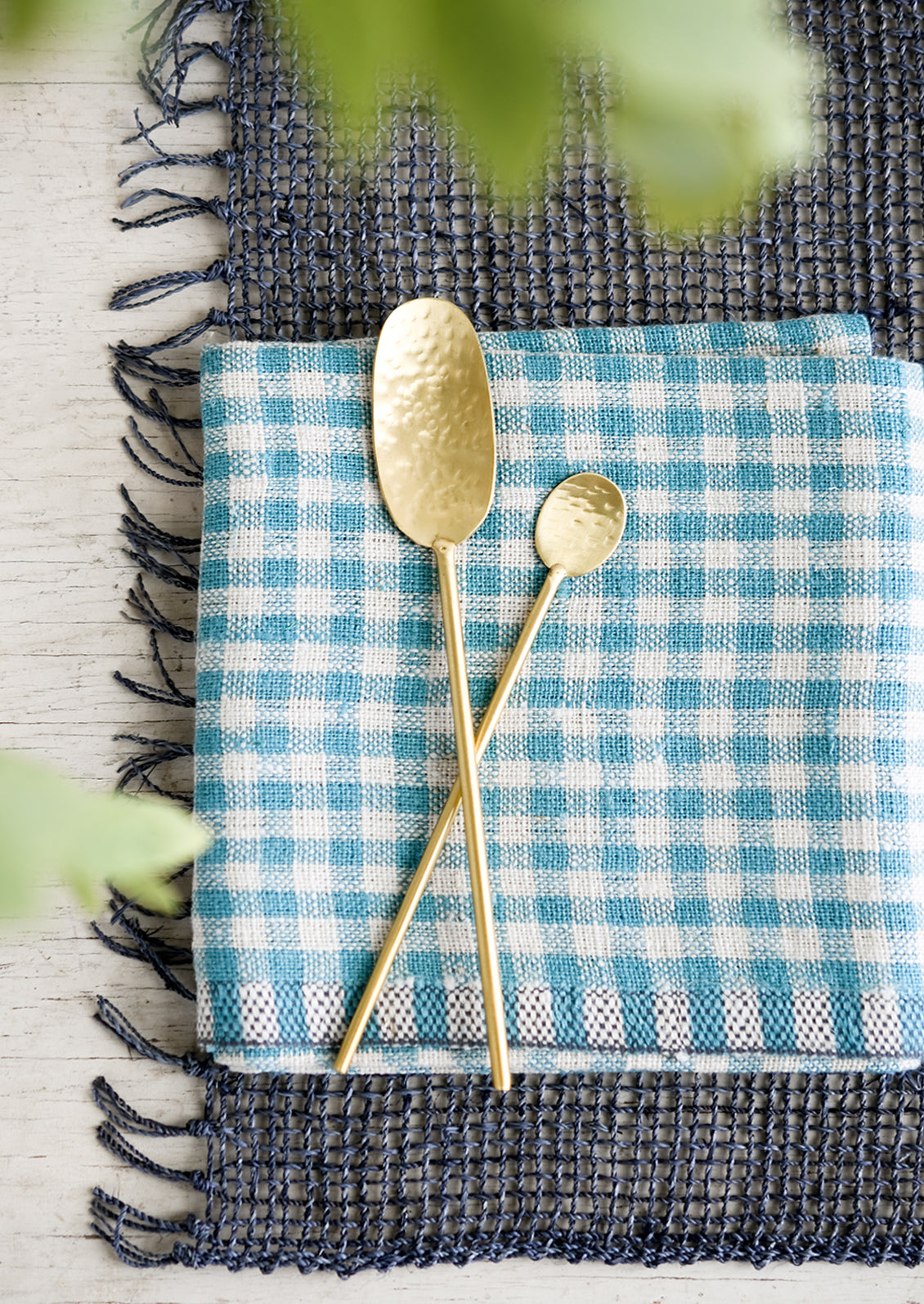 Hammered gold spoons on a blue gingham cloth.