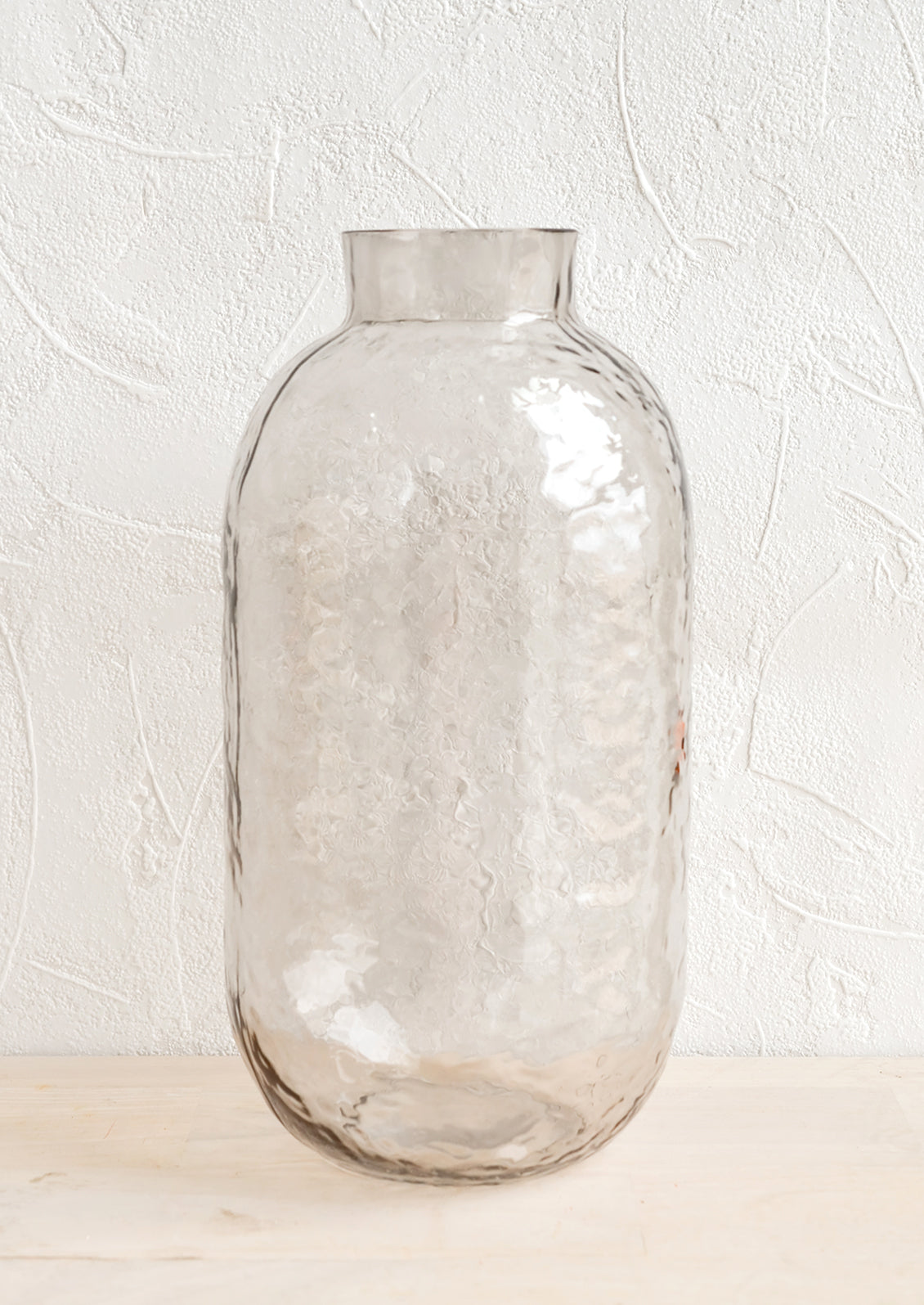 A tall glass vase with hammered texture in pale grey.