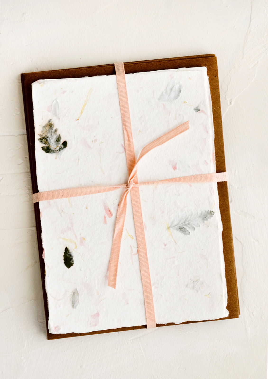 Handmade flower petal paper and kraft envelopes bound with peach ribbon.
