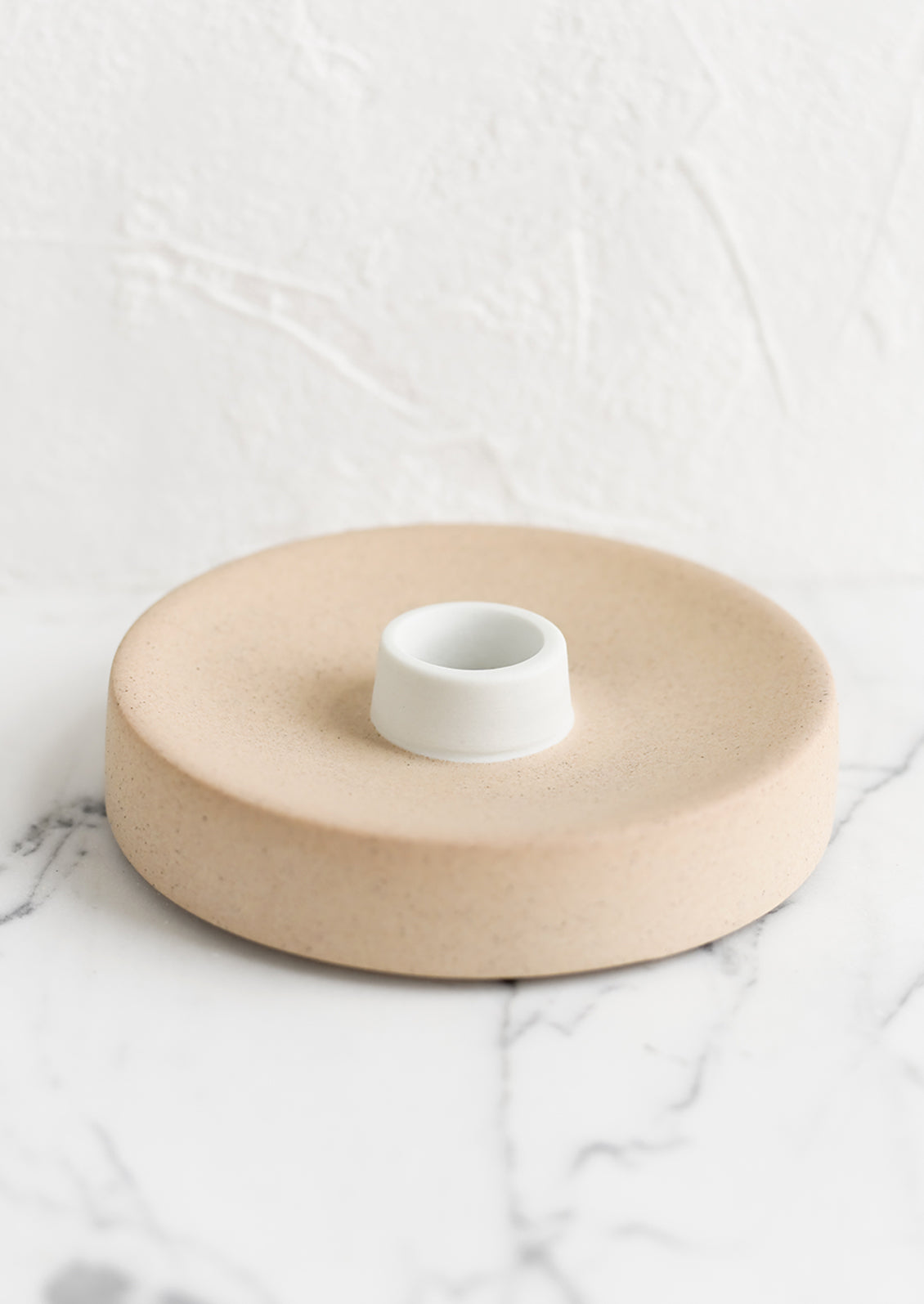 A round ceramic taper candle holder in sand.