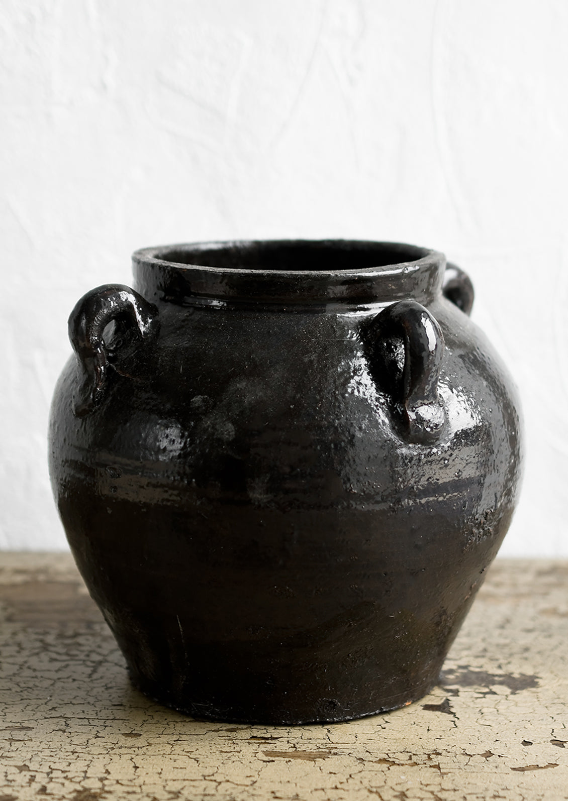 A dark brown (almost black) ceramic jar with decorative loop handles.