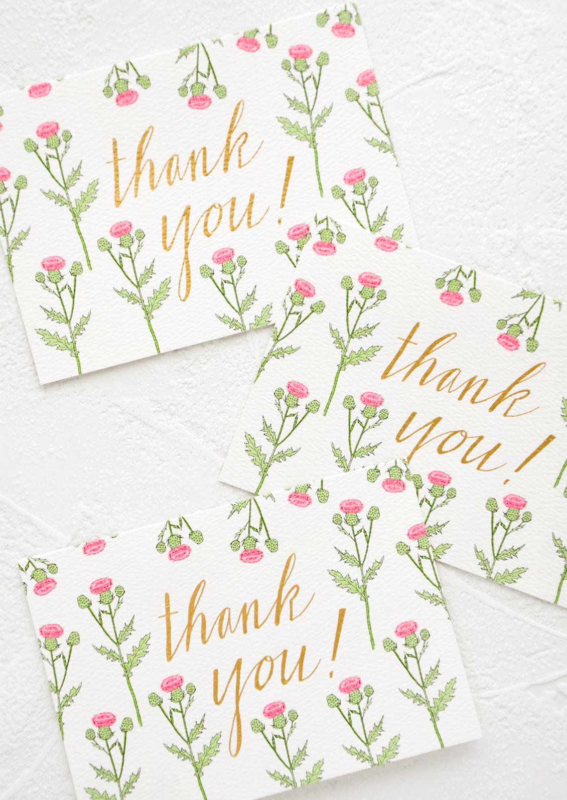 A set of identically printed thank you cards. Pink thistle print with gold "thank you!" in cursive.