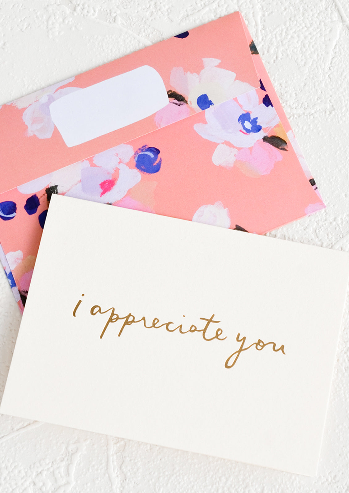 A white greeting card with golden cursive reading "I Appreciate You", paired with floral print envelope.