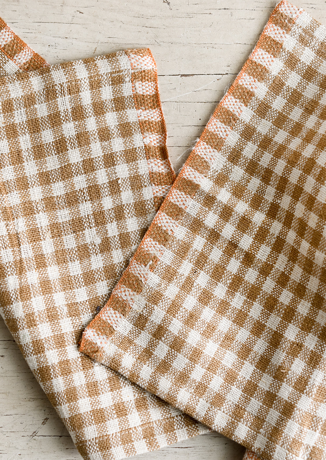 A pair of coffee brown gingham cocktail napkins with orange trim.