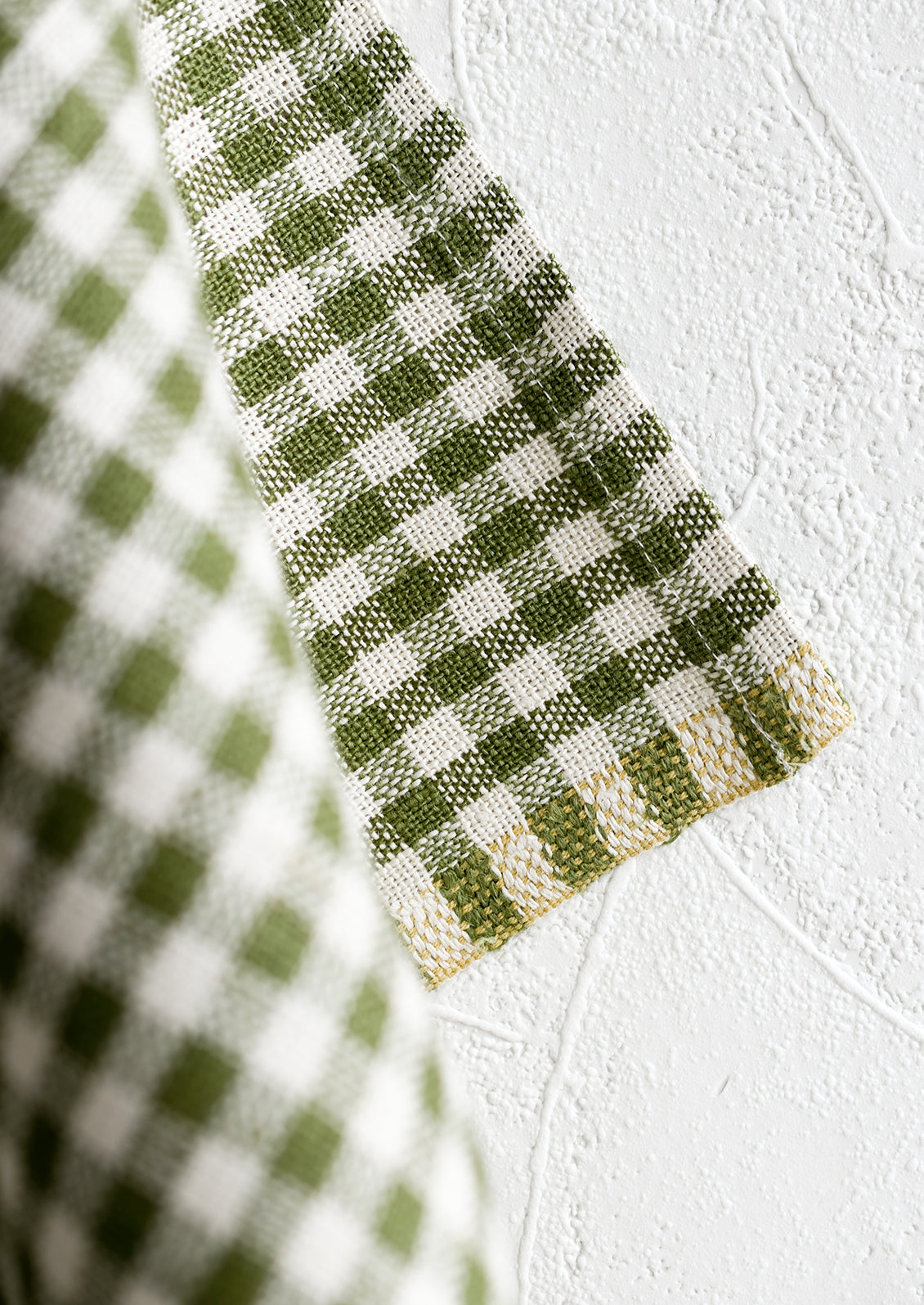 A woven gingham textile with contrast thread detailing along edge.