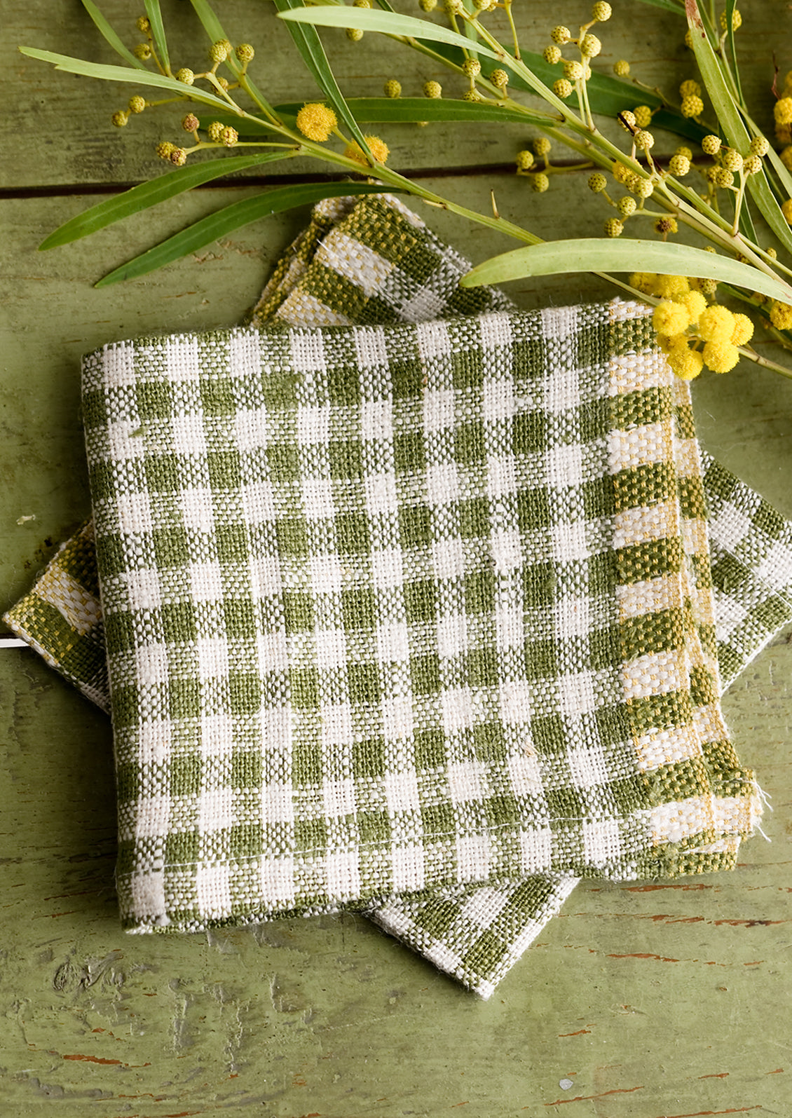 A pair of olive green gingham cocktail napkins.