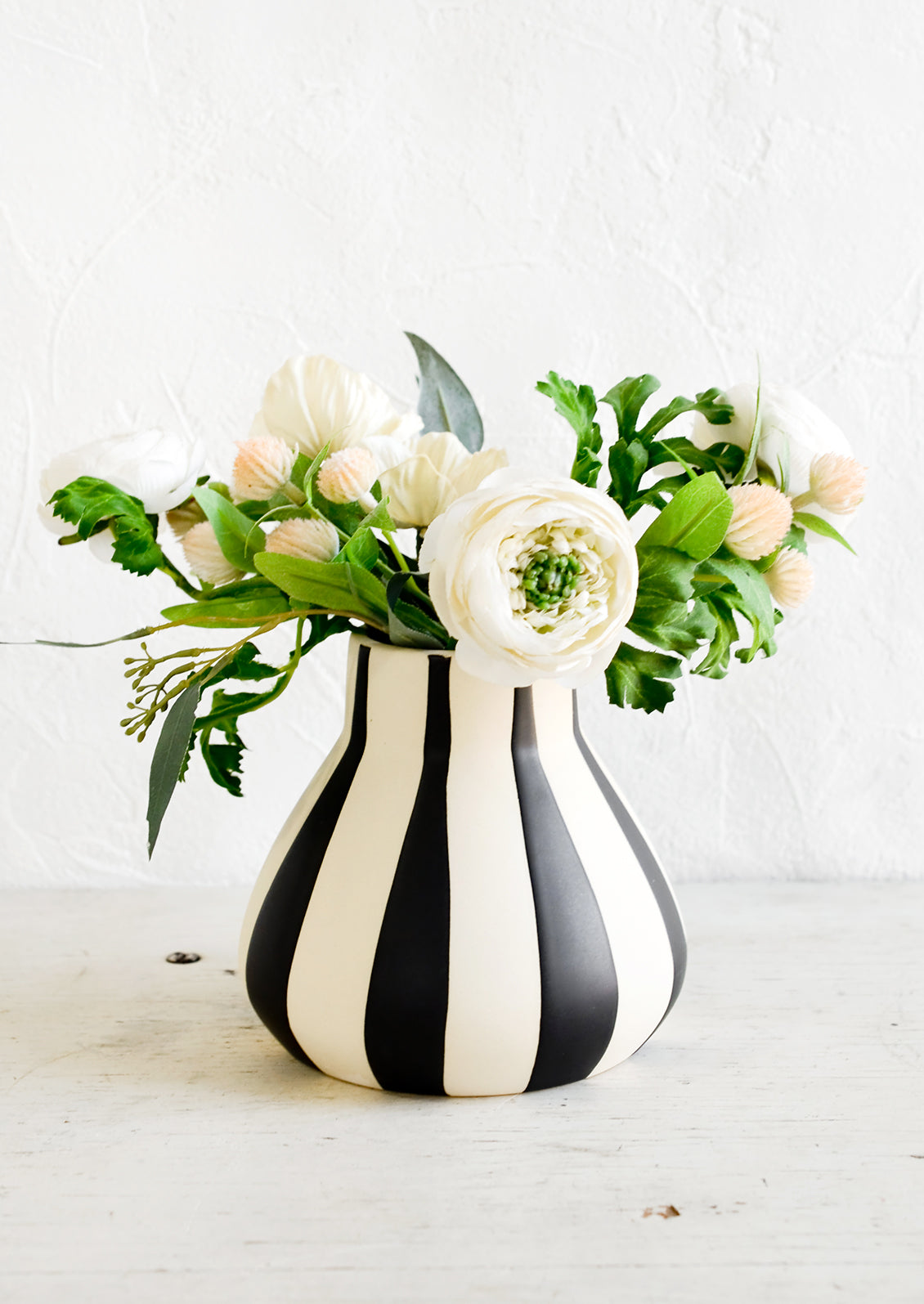 A flower arrangement in a white ceramic vase with thick black stripes.