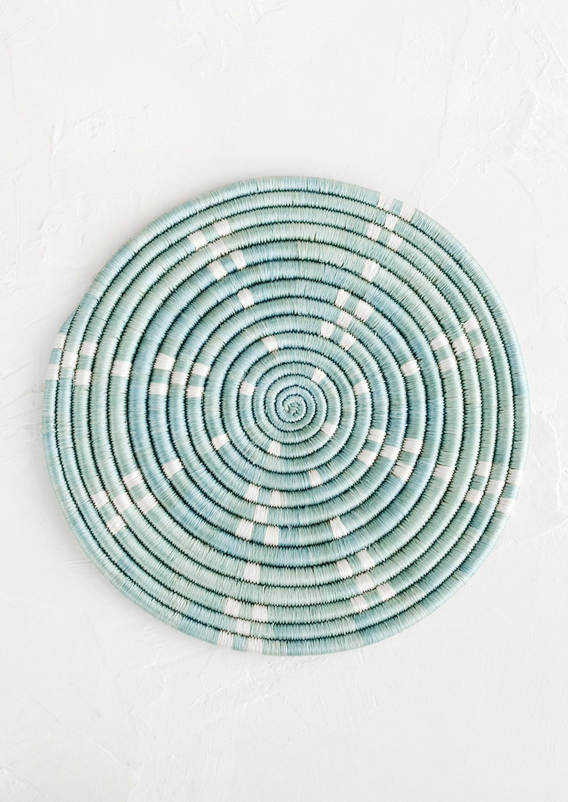 A round sweetgrass trivet in blue with white dash pattern.