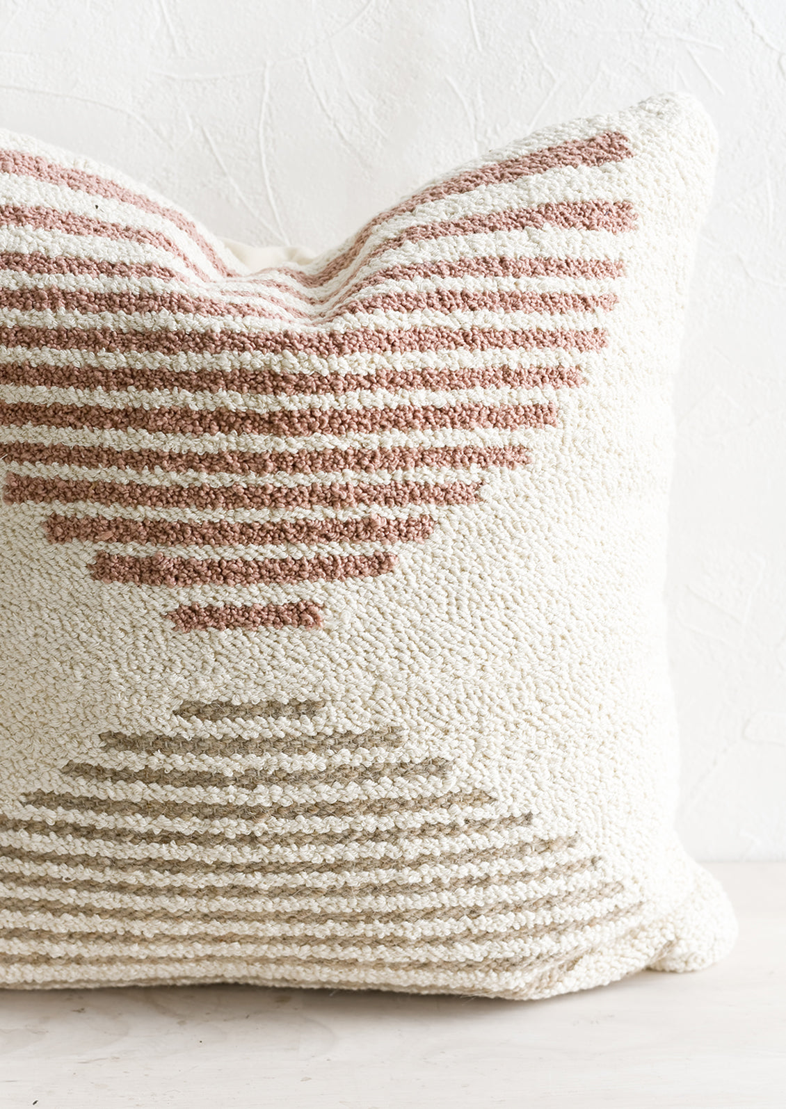 A tufted pillow in ivory with mauve and taupe geometric "horizon" design.