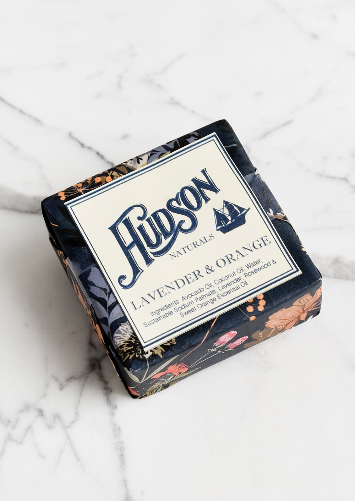 A square bar of soap in botanical printed packaging in Lavender & Orange scent.