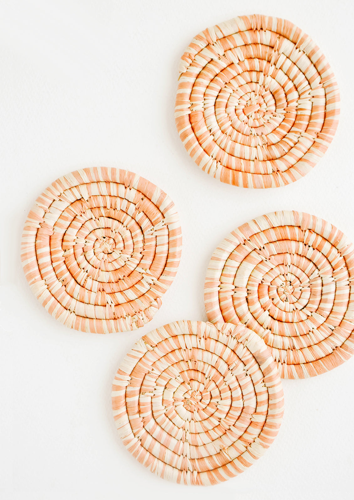 Set of 4 Round Woven Raffia Coasters in Peach and natural stripe.