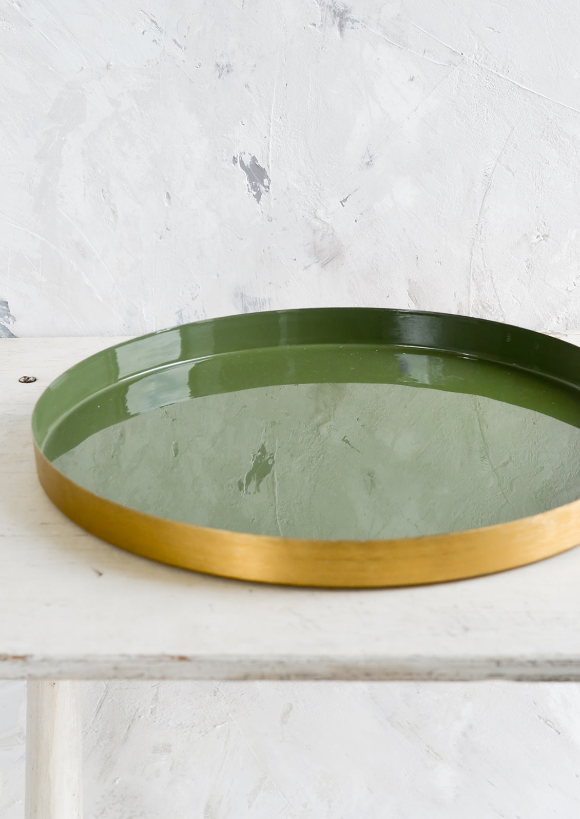 A large, round enamel tray with shallow brass rim and green interior.