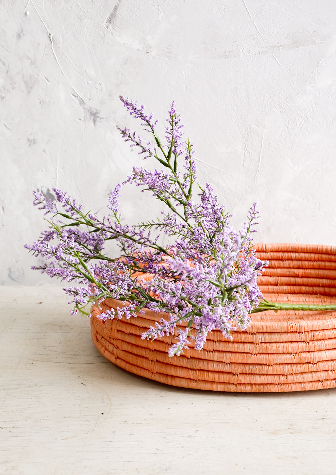 Woven raffia basket in peach color, housing purple flowers.