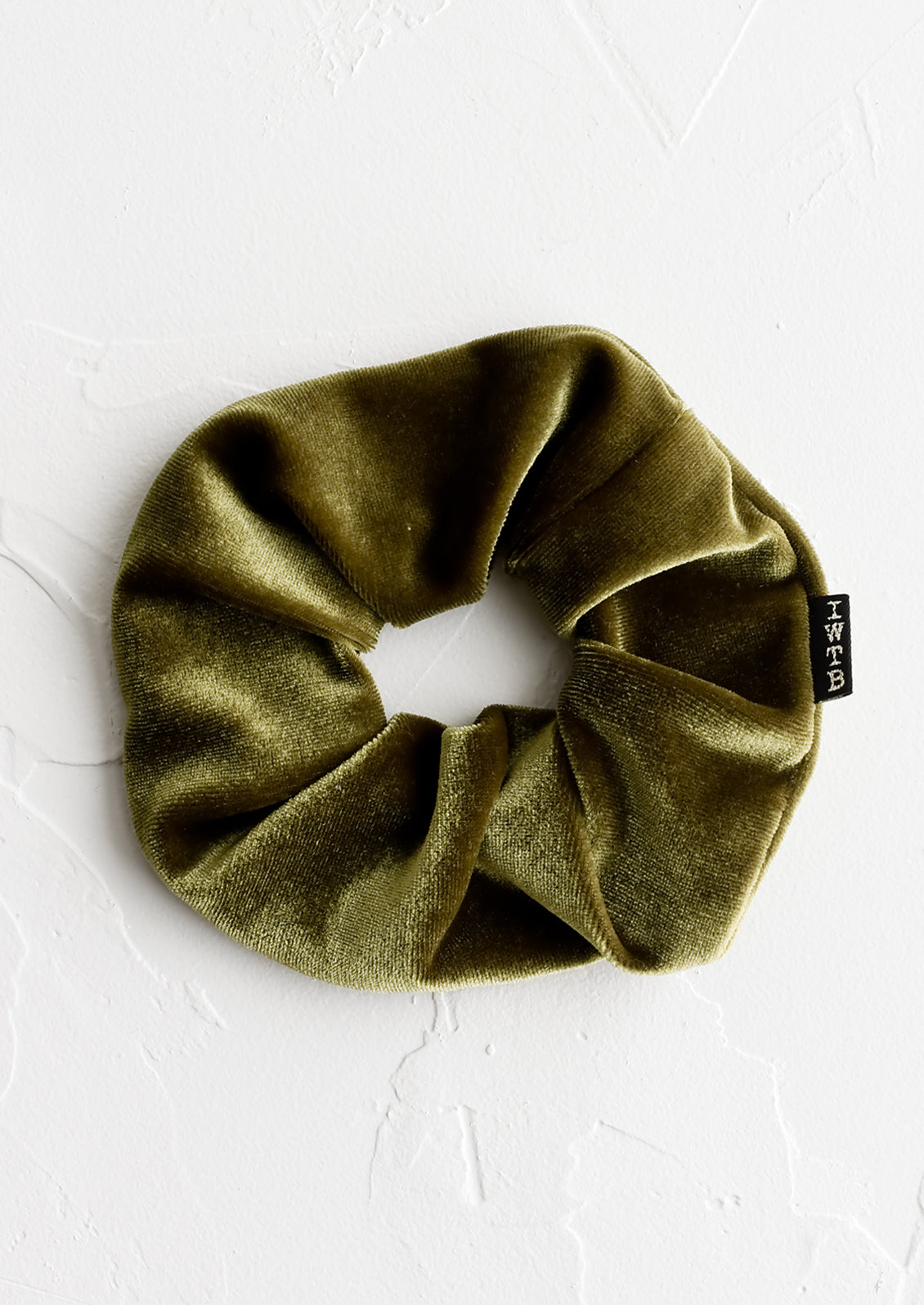 A velvet scrunchie in olive green with logo tag.