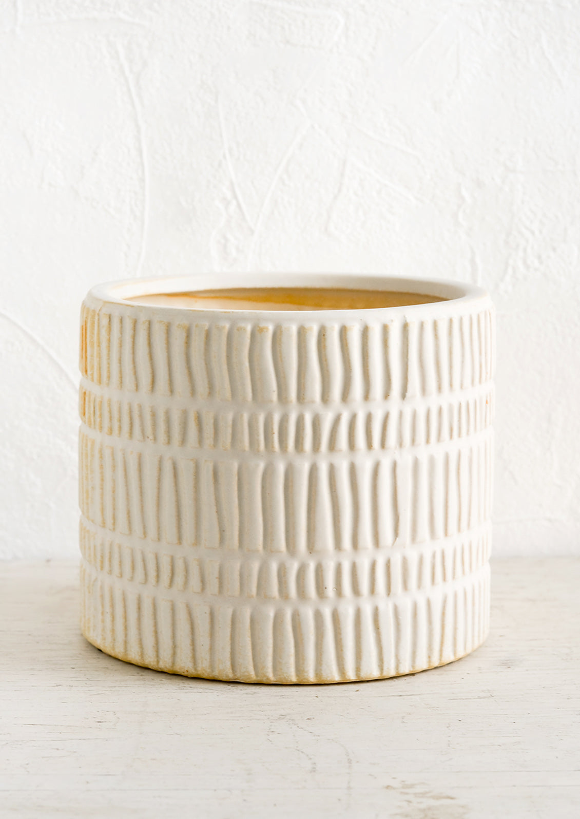 A bisque ceramic planter with rows of raised line texture throughout.