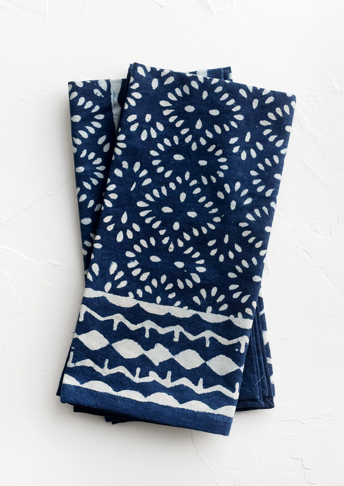 A pair of indigo napkins with white block printed pattern.
