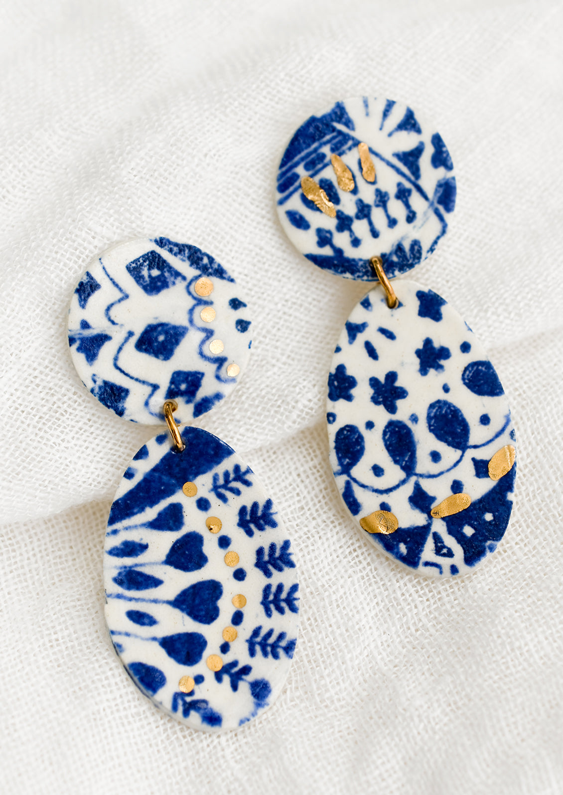 A pair of two-part ceramic earrings with indigo and gold leaf pattern.
