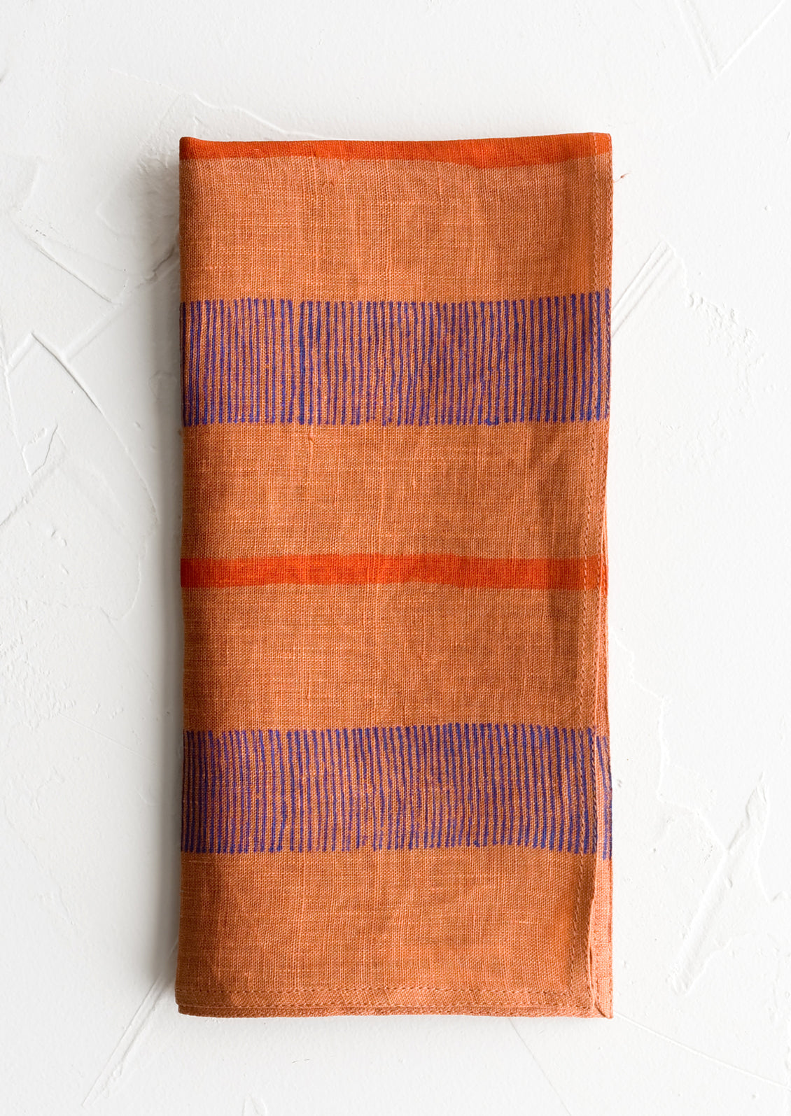 A terracotta linen napkin with block printed stripe design.