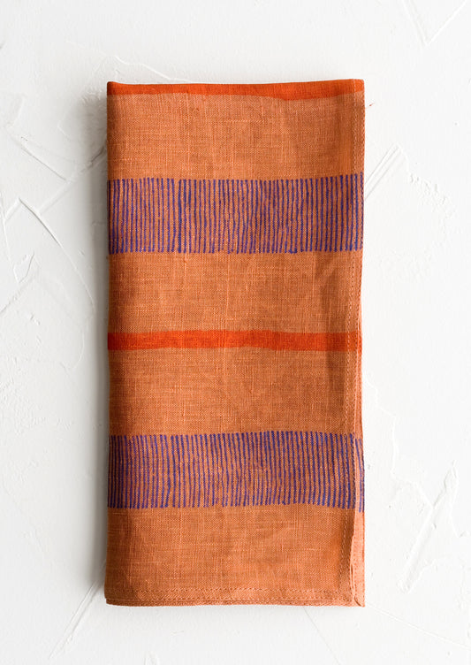 A terracotta linen napkin with block printed stripe design.