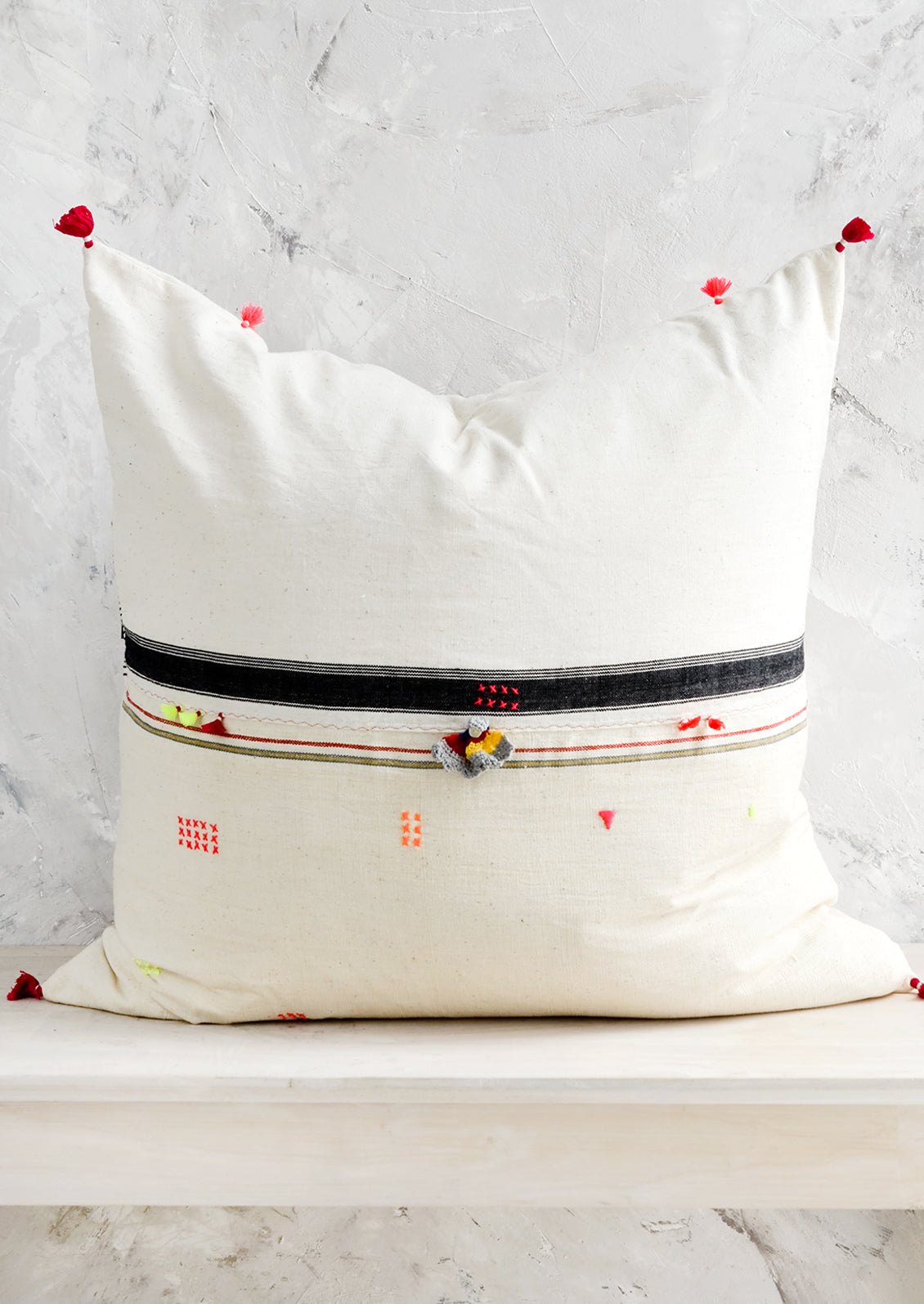 A square throw pillow with neon embroidery and tassel detailing.