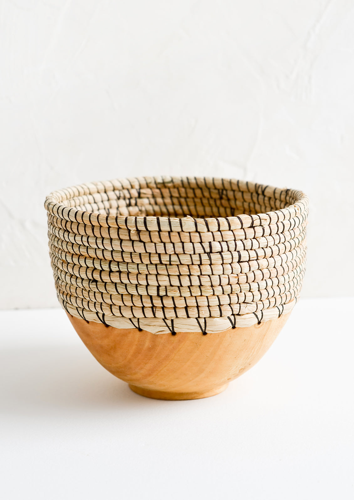 A small bowl made from half wood and half woven grass with black thread.