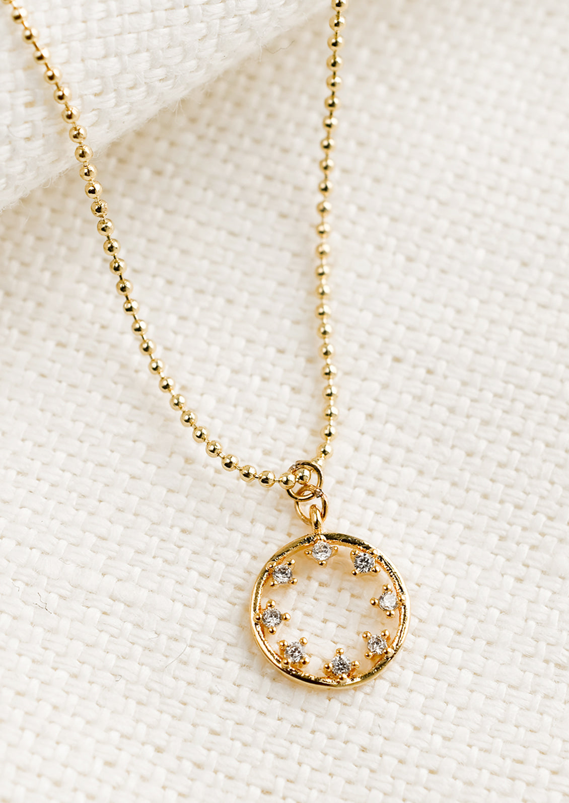 A gold necklace with circular pendant with clear inner stones.