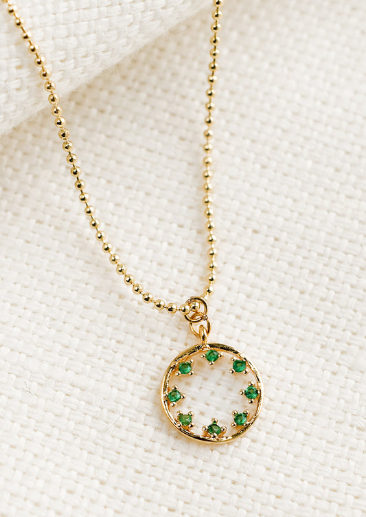 A gold necklace with circular pendant with green inner stones.
