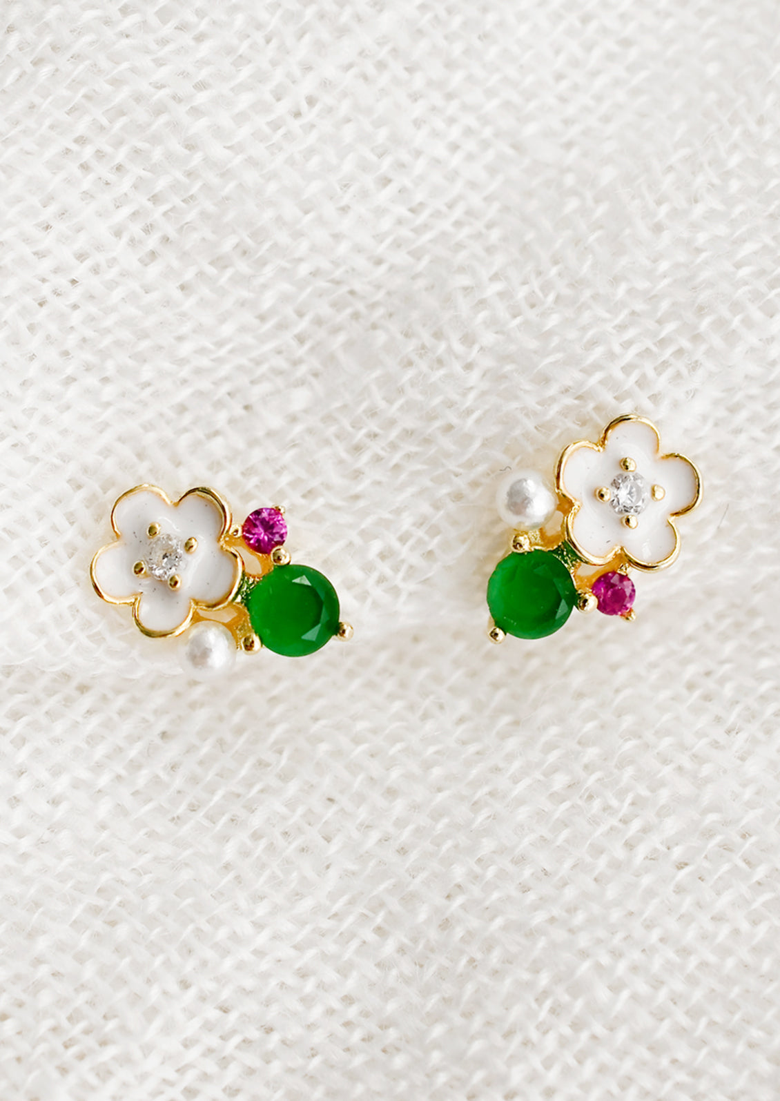 A pair of stud earrings with white flower and green and pink gems.