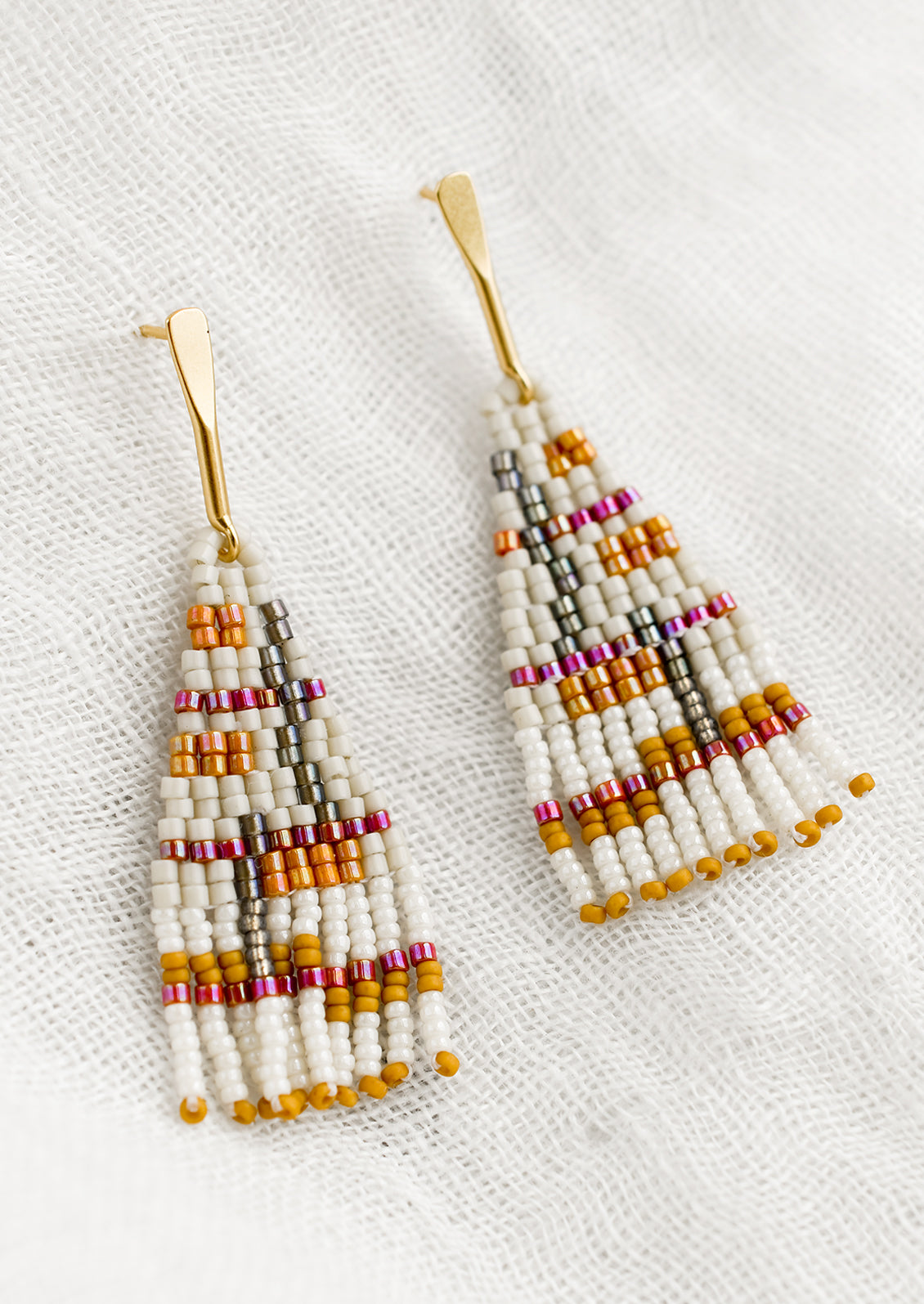 A pair of beaded earrings in neutral and magenta colorway.