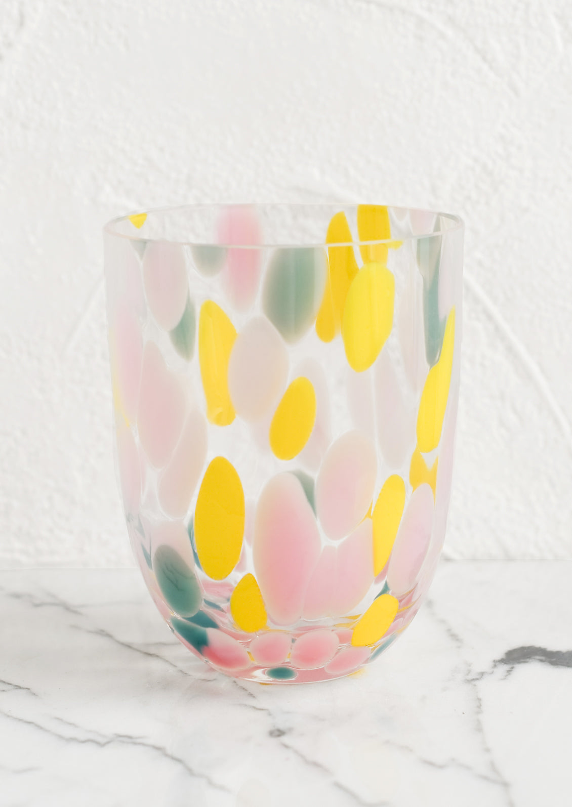 A handmade speckled glass juice cup with teal, yellow and pink spots.