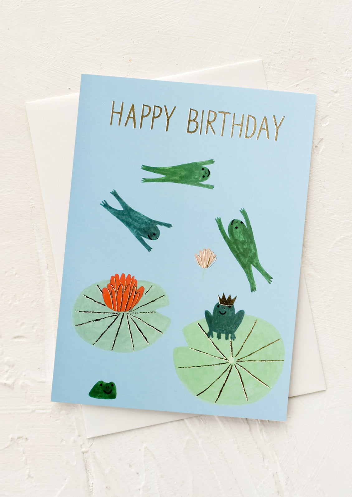 A greeting card with illustrated frogs jumping around on lilypads.